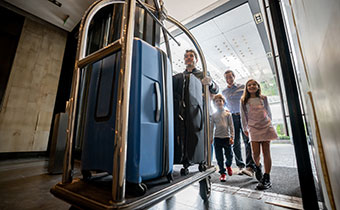 A family of 4 arriving at the hotel following a bellman with a luggage cart filled with luggage.